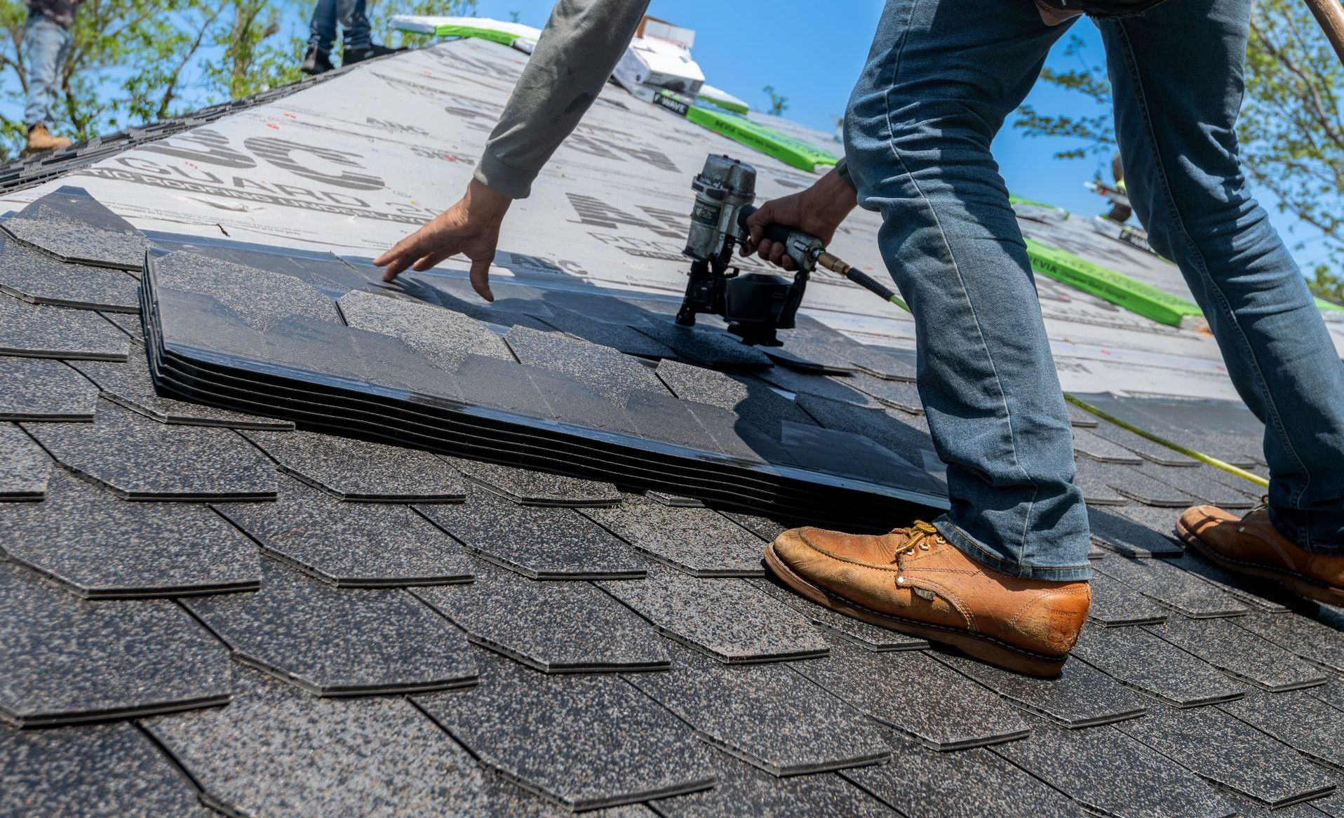 Roofer using nail gun for shingle installation on residential roof.