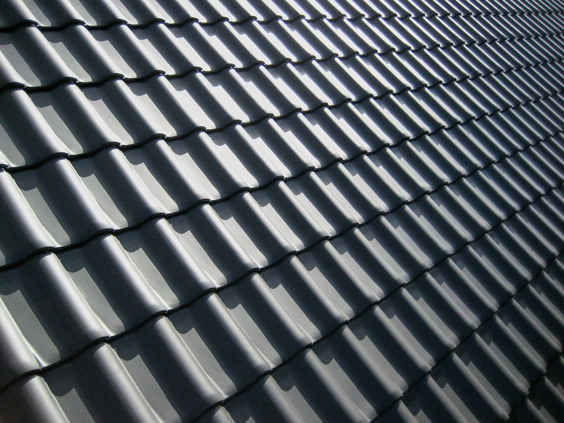 A pattern of dark grey roof tiles with sharp shadows in bright light